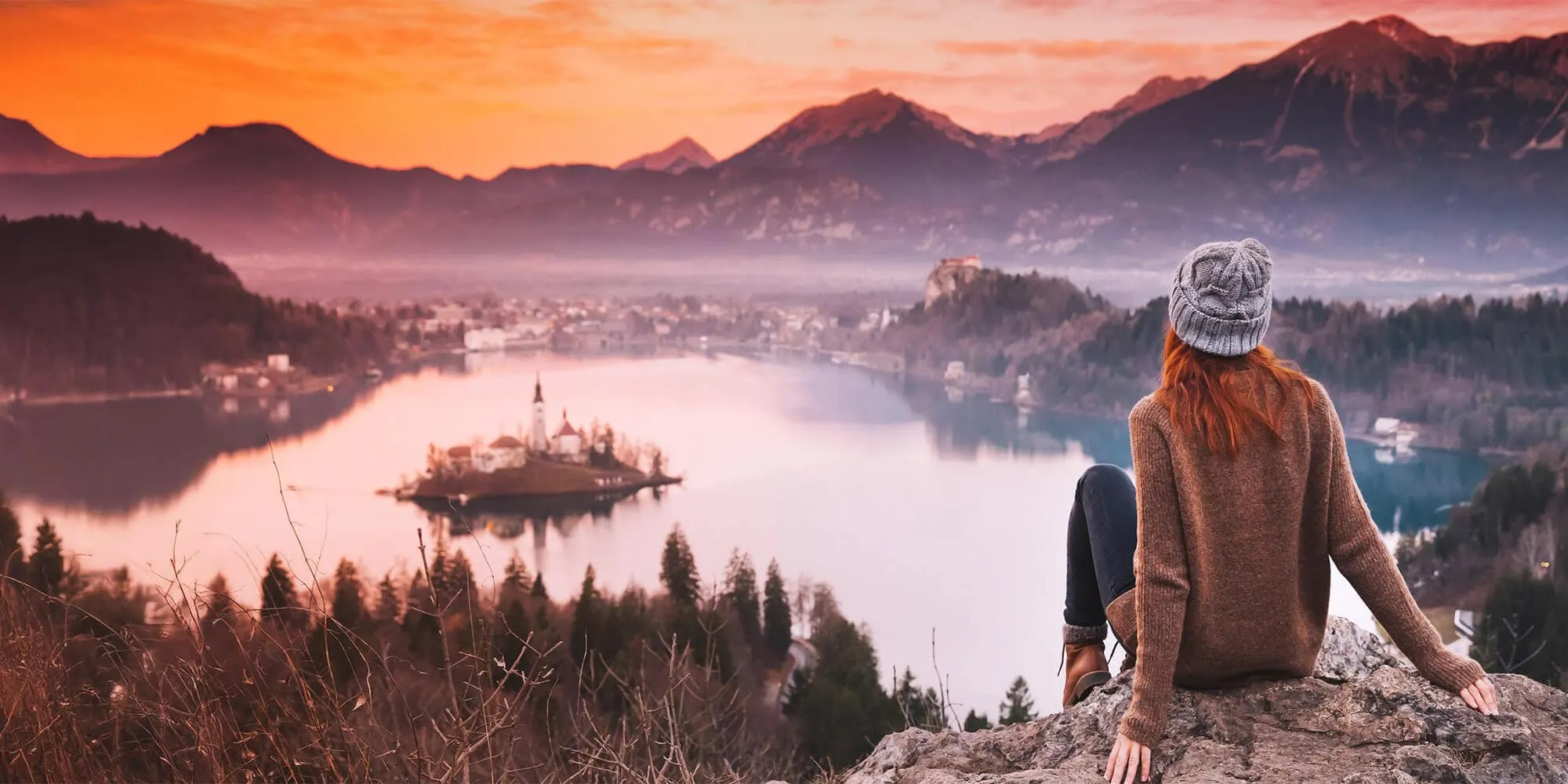 Reisende blickt bei Sonnenuntergang über den Bleder See und die slowenische Berglandschaft