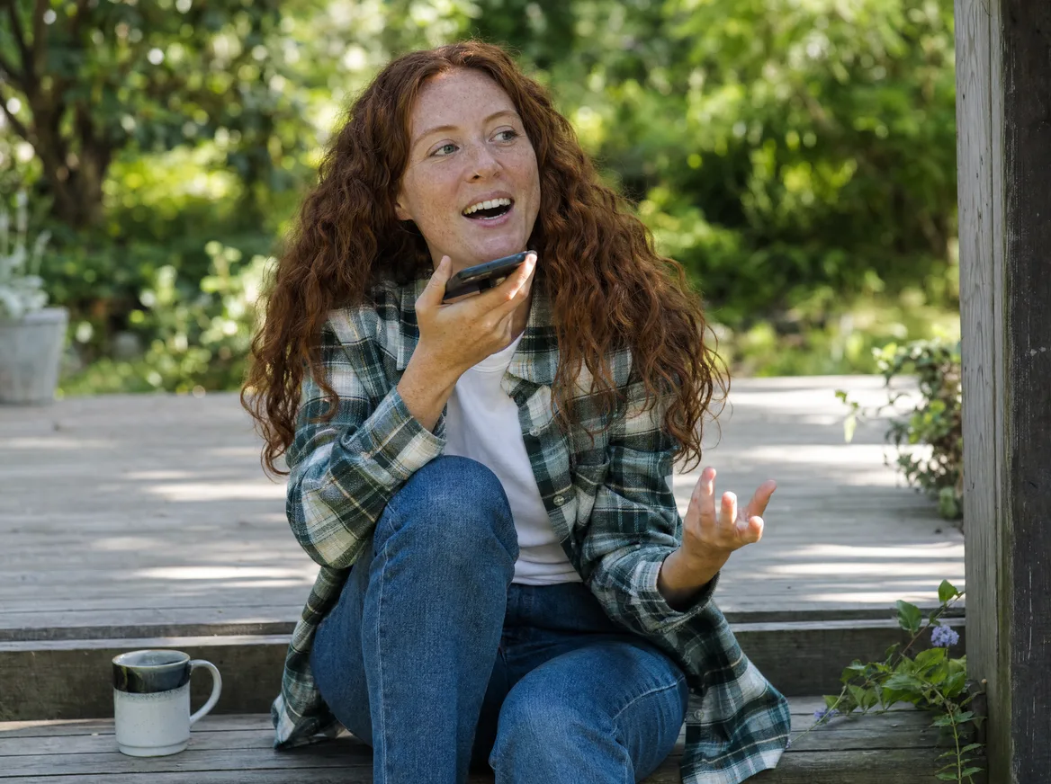 A young woman speaking her answer into her phone on the porch steps