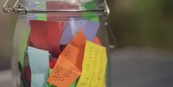 Glass jar filled with folded handwritten notes on colourful paper