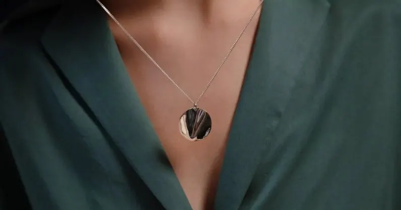 Round silver pendant on a fine chain worn over a green blouse
