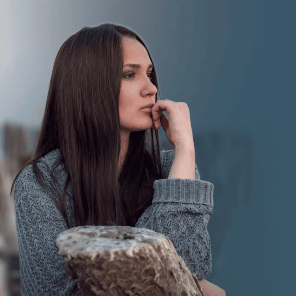 Woman in a grey knitted sweater sitting alone and looking into the distance, lost in thought