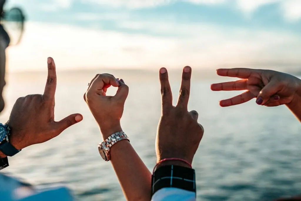 Four raised hands forming letters against the sea at sunset