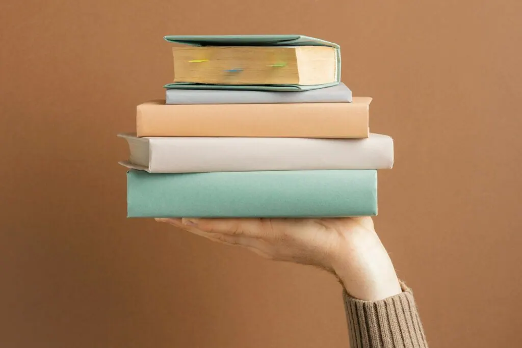 Hand hält einen Stapel gebundener Bücher in Pastellfarben vor braunem Hintergrund