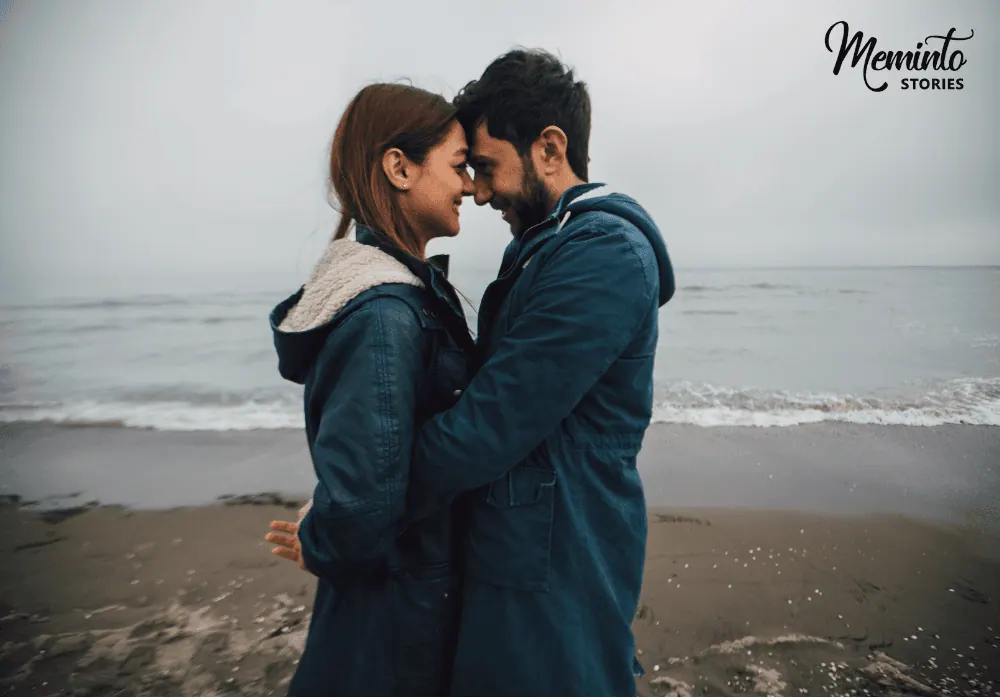 Couple in winter coats embracing forehead to forehead on a grey, misty beach