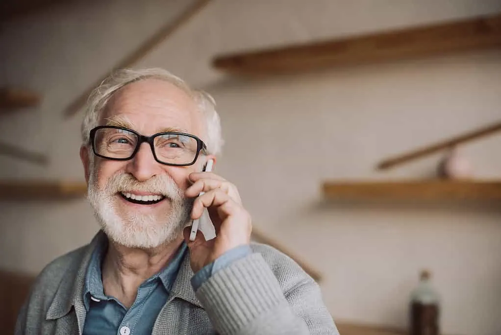 Älterer Mann mit Brille lacht, während er mit dem Smartphone telefoniert