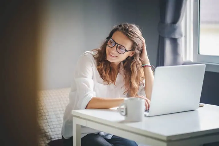 Frau mit Brille sitzt überlegend vor ihrem Laptop, daneben eine Kaffeetasse