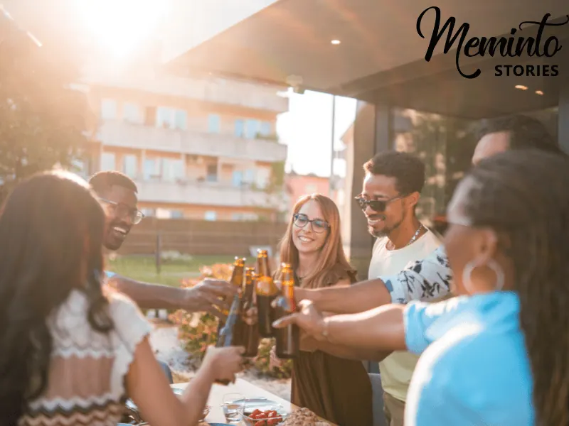 Friends clinking beer bottles around an outdoor table at a sunny farewell gathering