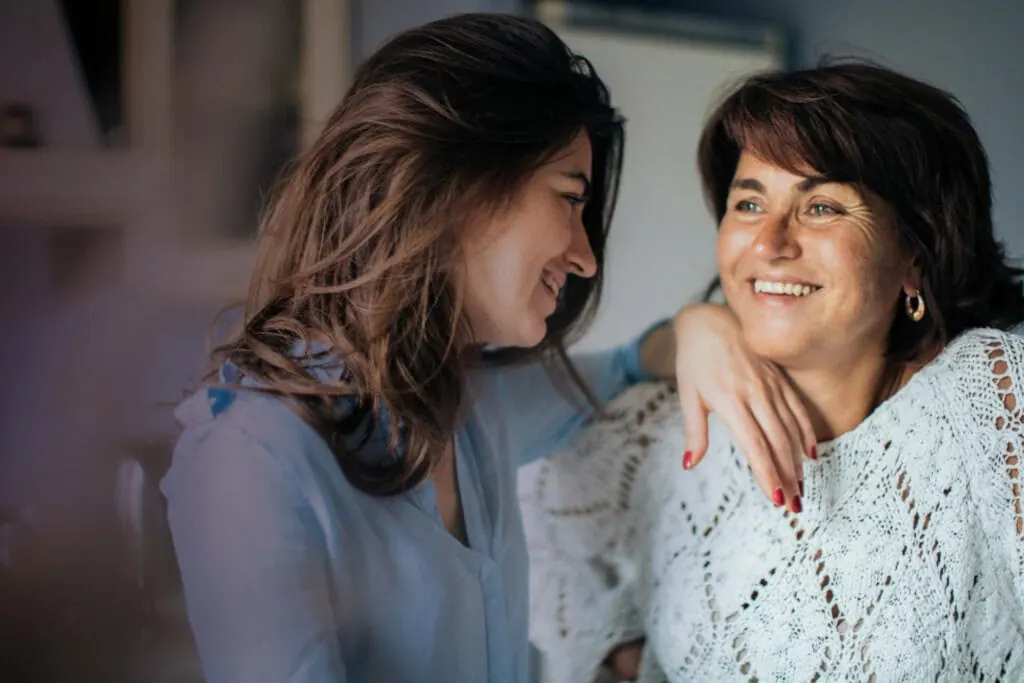 Two women sitting close together and smiling, one with an arm around the other's shoulder