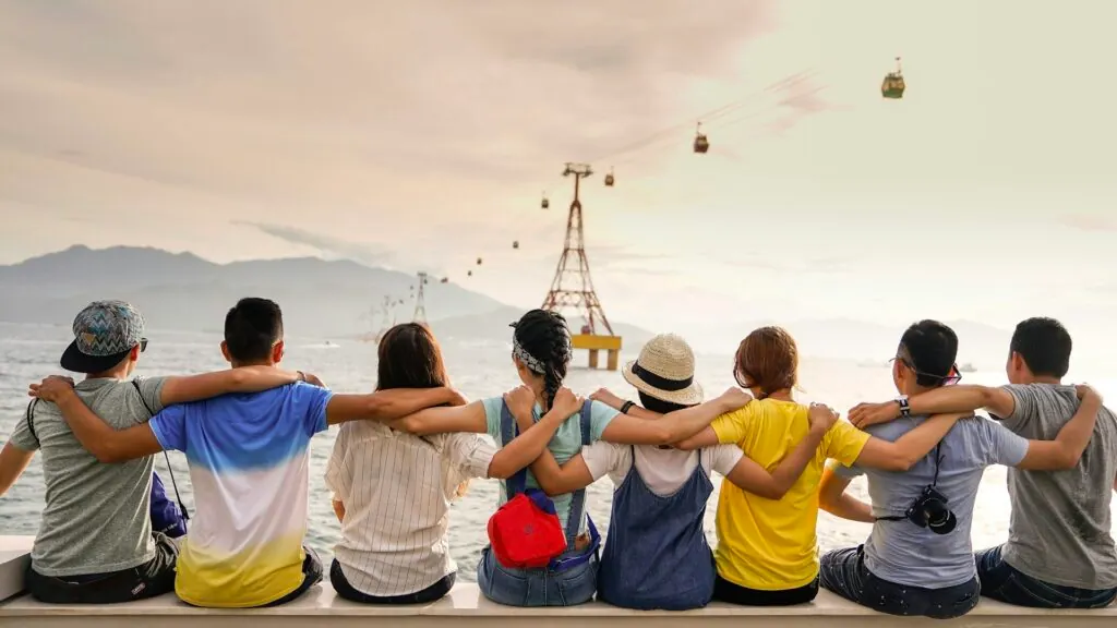 Group of friends sitting arm in arm on a wall, looking out over the water